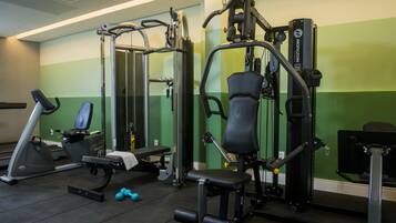 Un gimnasio con equipamiento de ejercicio, una banca y mancuernas.