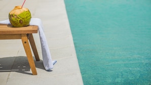 A poolside area with a lounge chair, a table with a coconut drink, and umbrellas. - Hotel Luzeiros Recife (Recife)