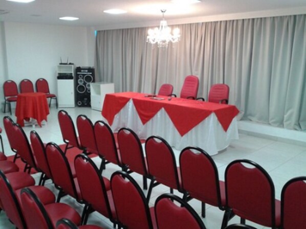 Un salón de conferencias con una larga mesa cubierta con un mantel rojo, rodeada de sillas rojas.