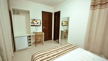 Een hotelkamer met een bed, een bureau, een stoel, een kledingkast en een spiegel.