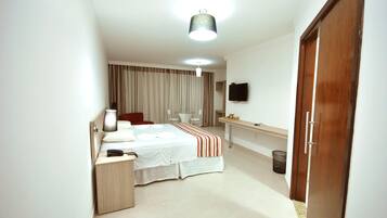 Quarto de hotel com cama, mesa de cabeceira, abajur e televisão presa na parede.