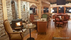 A cozy interior with a stone wall, a fireplace, wooden furniture, and a dining area. - Willa Pokusa - Szczawnica (Szczawnica)