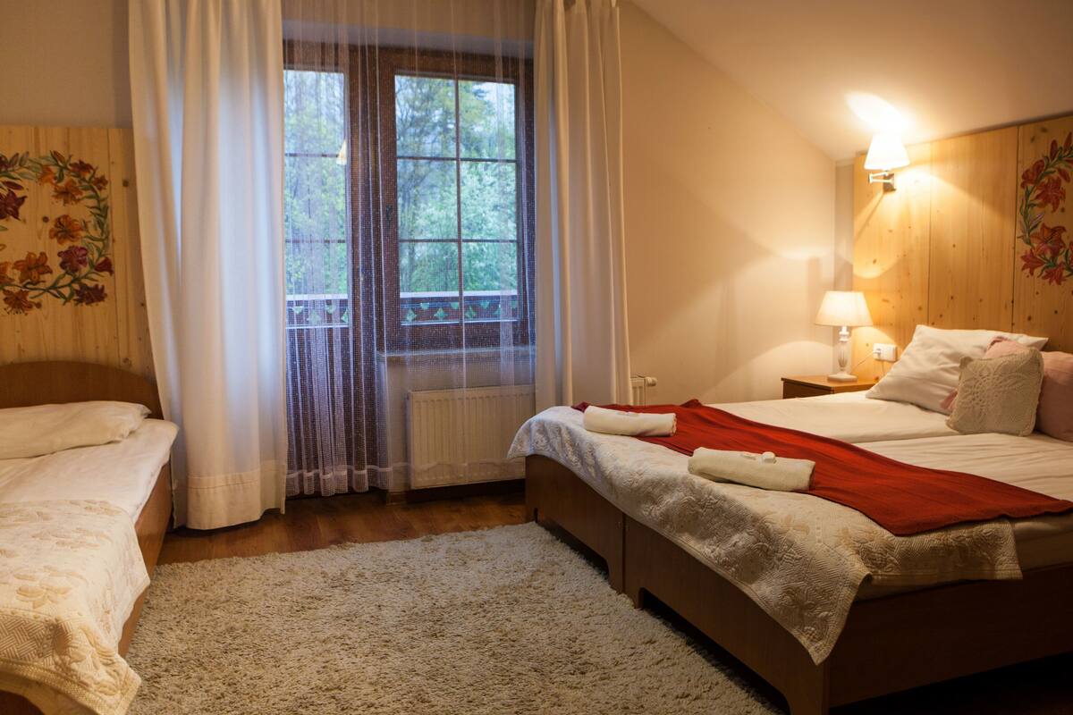 Ein Hotelzimmer mit zwei Betten, einem großen Fenster mit Vorhängen, einem Holzboden und einer Wandlampe.