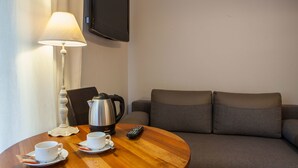 A hotel room with a round wooden table, a white lamp, a black coffee maker, a remote control, and a grey sofa. - Willa Pokusa - Szczawnica (Szczawnica)