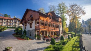 A traditional wooden building with a balcony, stone foundation, and outdoor seating area. - Willa Pokusa - Szczawnica (Szczawnica)