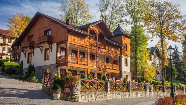 A traditional wooden building with a balcony, stone wall, and potted plants. - Willa Pokusa - Szczawnica (Szczawnica)