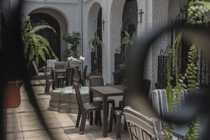 An outdoor patio with tables and chairs, surrounded by potted plants and a white wall with arches. - Hotel Ajau Colonial (Guatemala City)