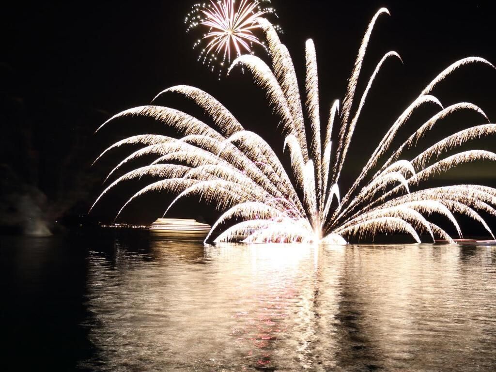 A nighttime view of fireworks over a body of water with reflections on the surface.