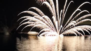A nighttime view of fireworks over a body of water with reflections on the surface.