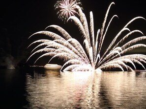 A nighttime view of fireworks over a body of water with reflections on the surface. - Toya Gokirakutei (Toyako)