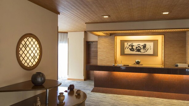 A reception area with a wooden reception desk, a framed artwork on the wall, and a traditional Japanese-style window. - Toya Gokirakutei (Toyako)
