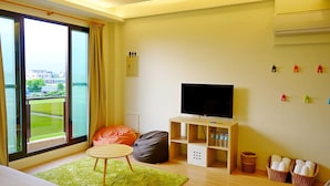 A modern hotel room with a large window, a flat-screen TV, a green rug, a bean bag, a wooden TV stand, and a small table. - Green Field & Sunshine (Luodong)