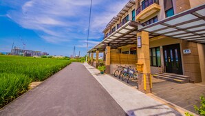A modern building with a covered entrance, a bike parking area, and a pathway leading to a green field. - Green Field & Sunshine (Luodong)