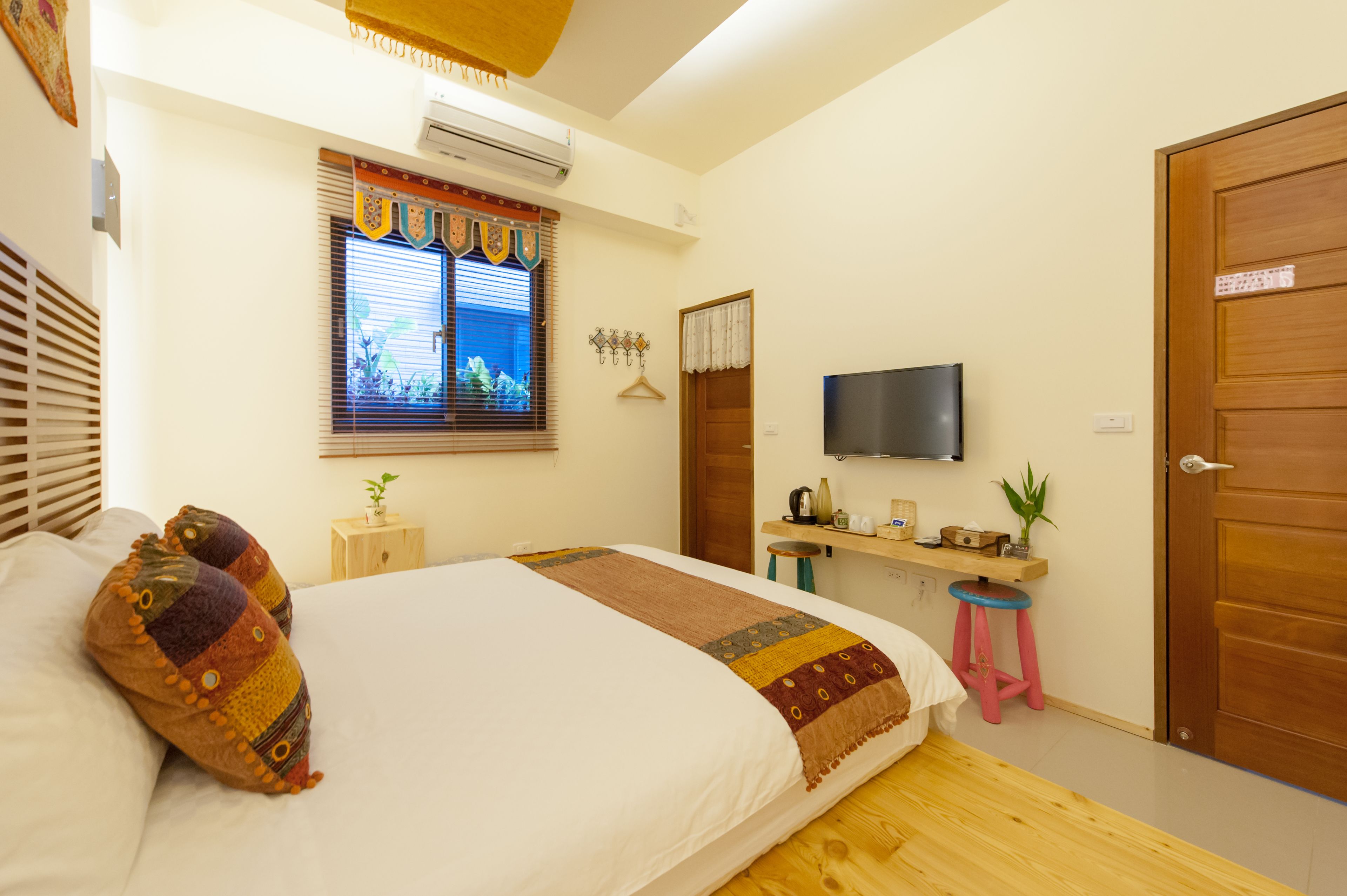 A neatly arranged bedroom with a bed, a television, a small desk, and a window with blinds.