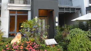 Ein modernes Gebäude mit Balkonen, ein kleiner Garten mit rosa Blüten und ein Gebäude mit einem Reetdach.