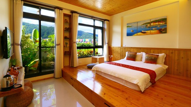 Ein geräumiges Schlafzimmer mit einem großen Bett, Holzboden, Fernseher und einem Fenster mit Blick auf Grünflächen und Berge.