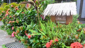 Ein Garten mit einem strohgedeckten Gebäude, auf dem „Post“ steht, umgeben von üppigem Grün und blühenden Pflanzen.