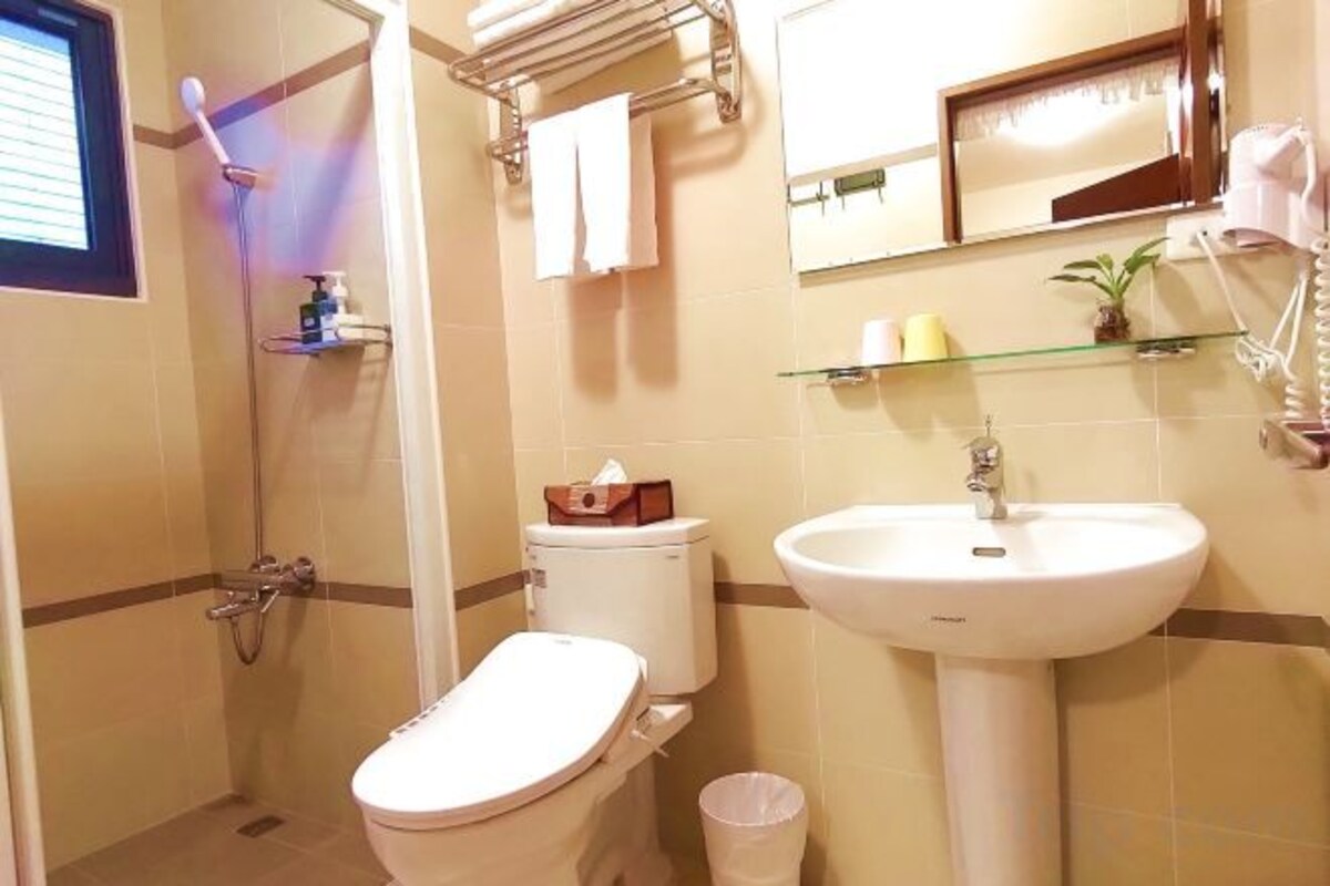 Un baño con inodoro, lavabo y ducha. Hay un perchero y un espejo sobre el lavabo.