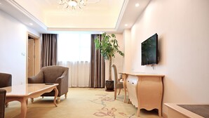 A hotel room with a flat-screen TV mounted on the wall, a wooden desk, a chair, a sofa, and a large potted plant. - Royal International Hotel Disneyland and Wild Animal Park Branch (Shanghai)