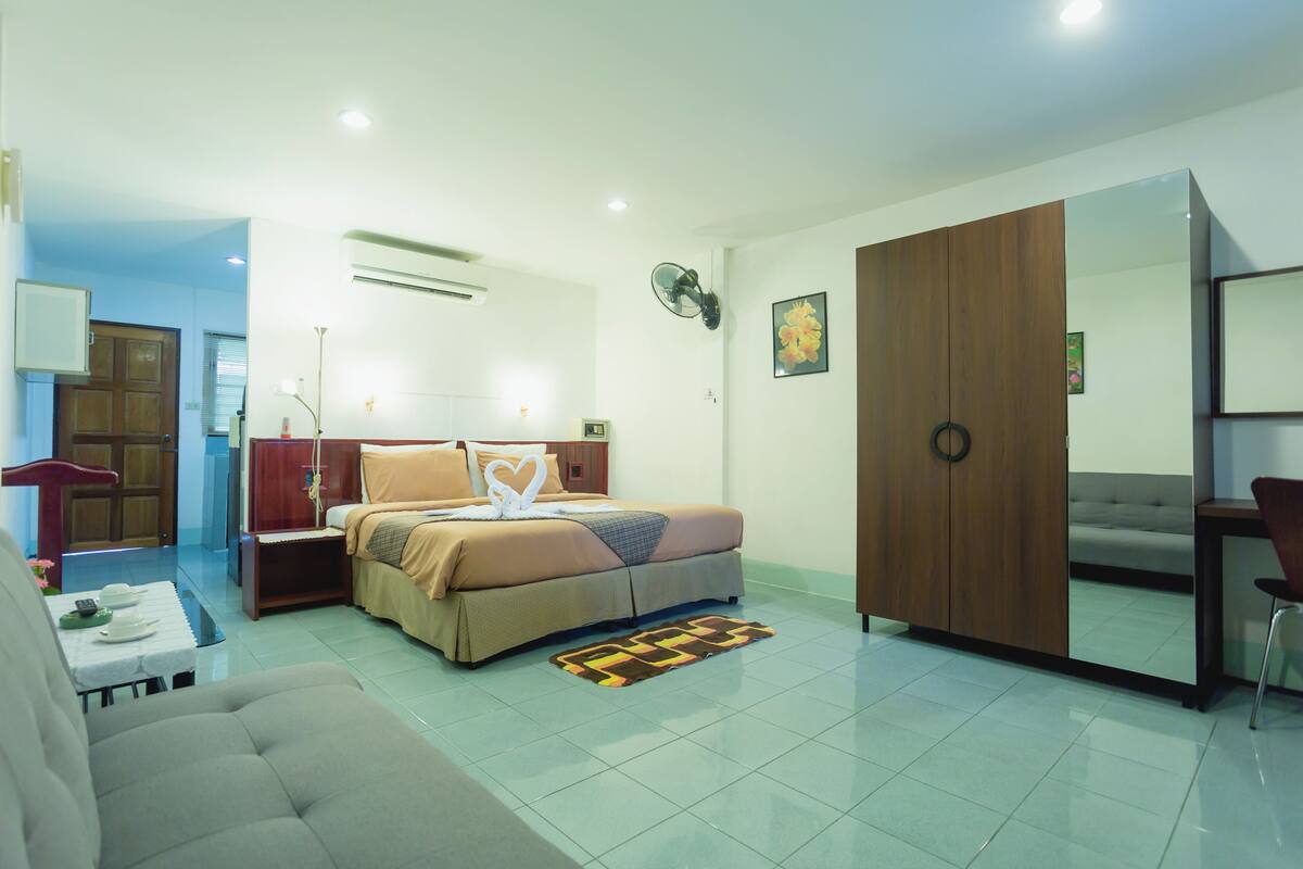 A modern hotel room with a bed, a sofa, a desk, and a wardrobe.