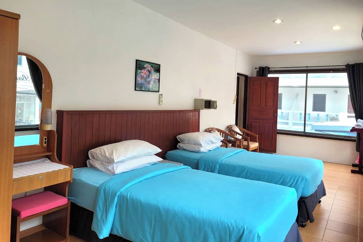 A hotel room with two beds, a wooden desk, a chair, a window with curtains, and a painting on the wall.