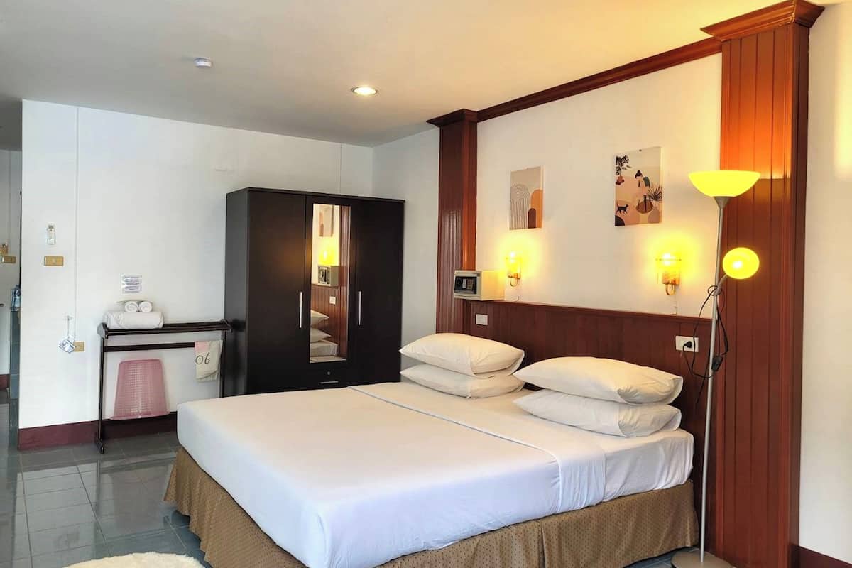 A hotel room with a bed, a wardrobe, a desk with a chair, and a lamp.