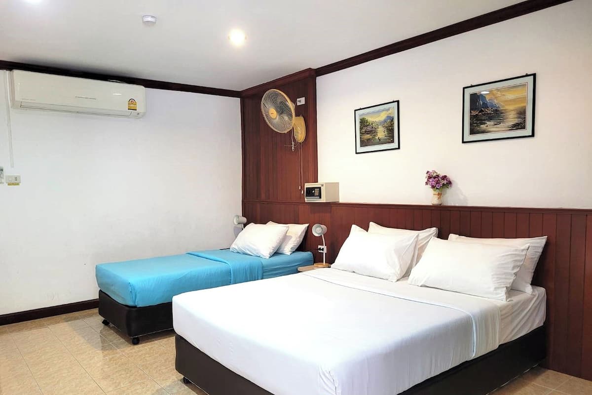 A hotel room with a large bed, a smaller bed, a bedside table, a lamp, a wall-mounted air conditioner, and two framed pictures on the wall.