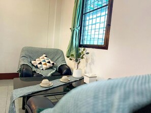 Une pièce chaleureuse avec un fauteuil vert, une petite table sur laquelle sont posées des tasses et des soucoupes, et une plante en pot.