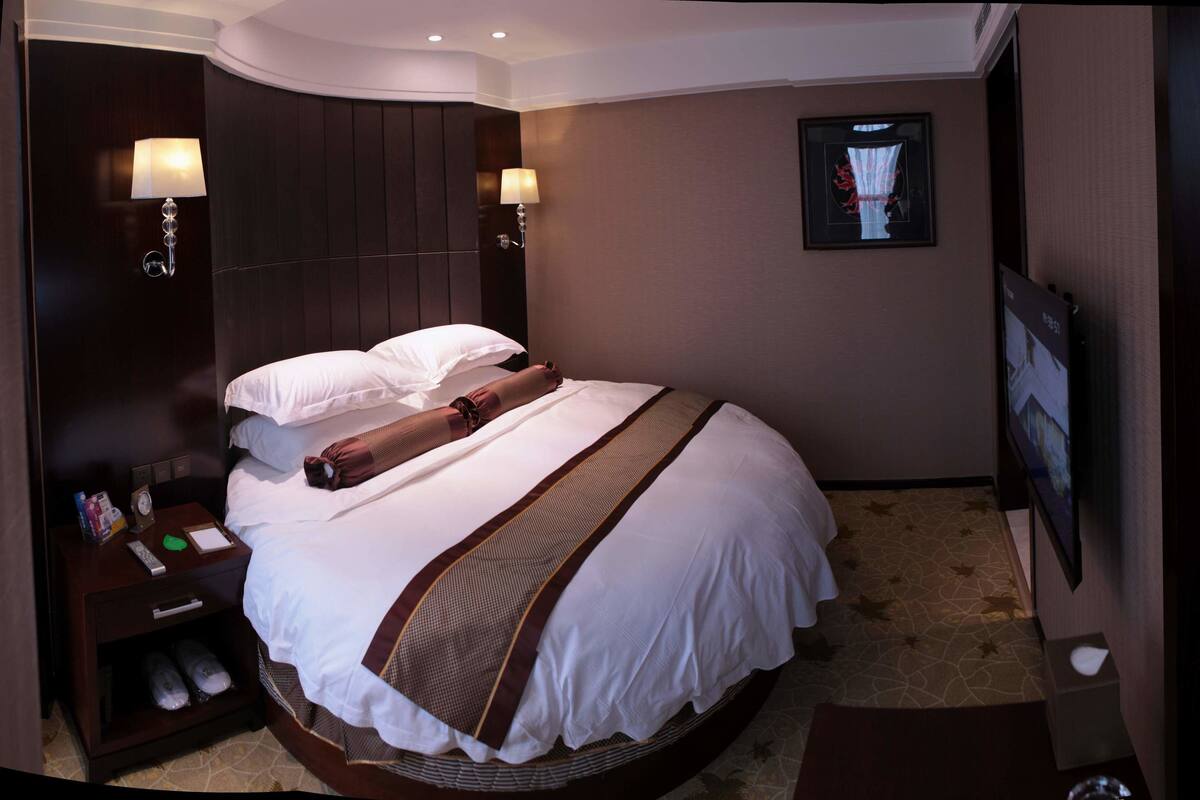 Habitación de hotel con una cama grande, dos lámparas de noche, un cuadro en la pared y un televisor a la derecha.