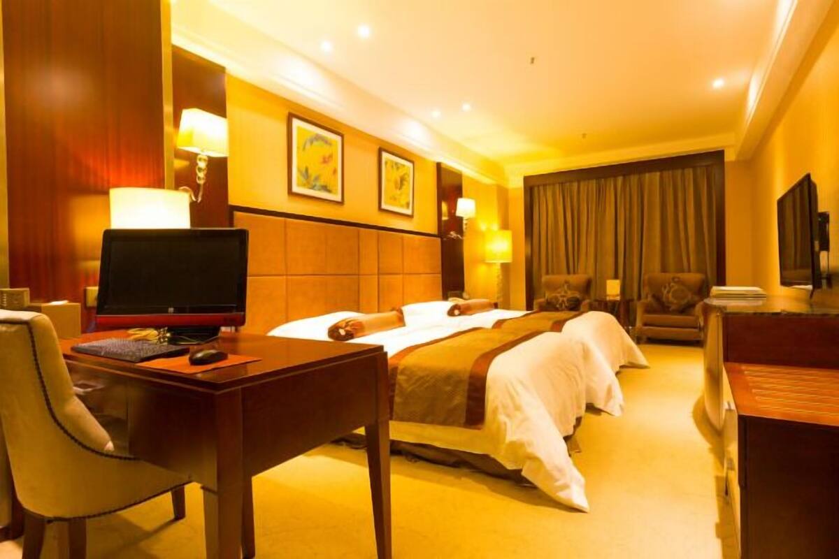 Habitación de hotel con cama, escritorio con computadora, silla, televisor y lámpara.