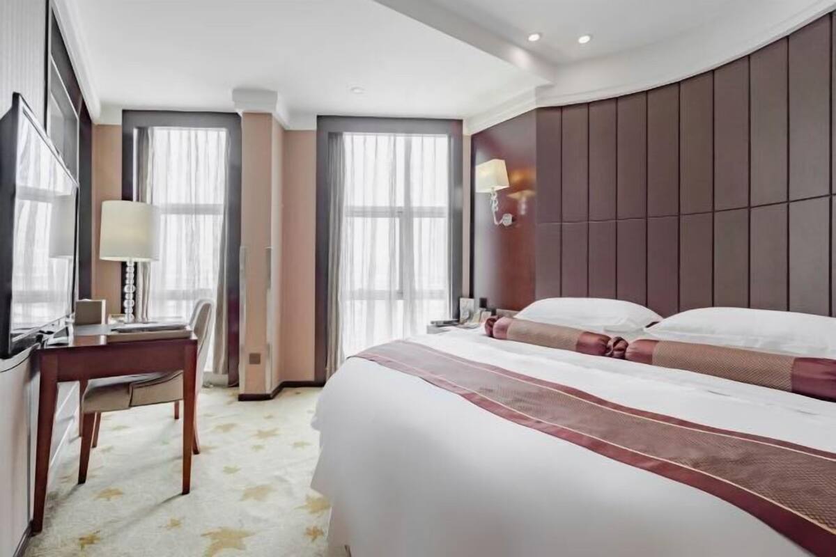 Habitación de hotel con una cama grande, un escritorio con silla, un televisor y una ventana con cortinas.