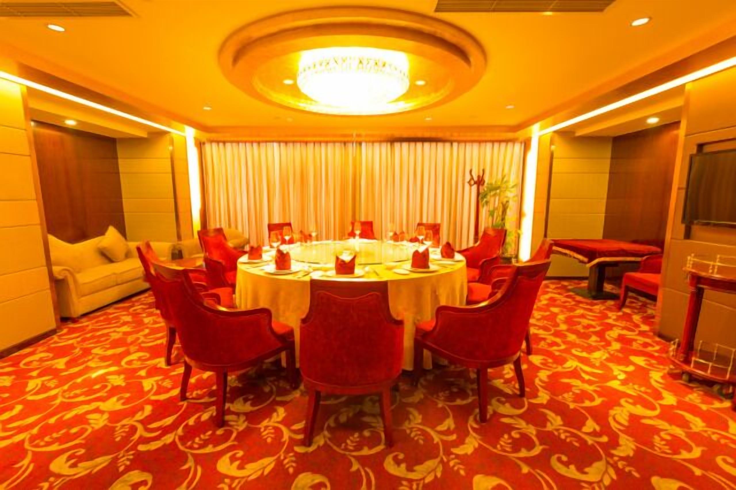 A conference room with a round table, red chairs, and a chandelier.