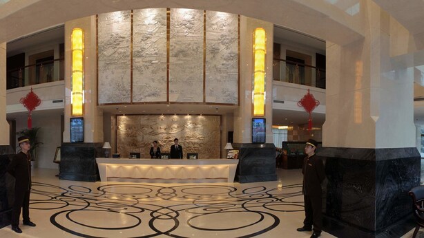 A lobby with a reception desk, two attendants, a large decorative wall, and a patterned floor. - Chengdu Gaoyi Hotel (Chengdu)