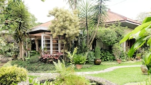 Una casa rodeada de vegetación exuberante, un pequeño estanque y un sendero.