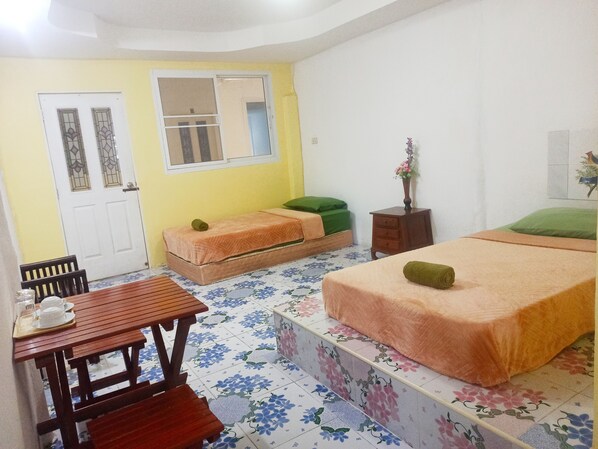 Una habitación con dos camas, una mesa de madera con una silla, un armario pequeño y una ventana con vistas al exterior.