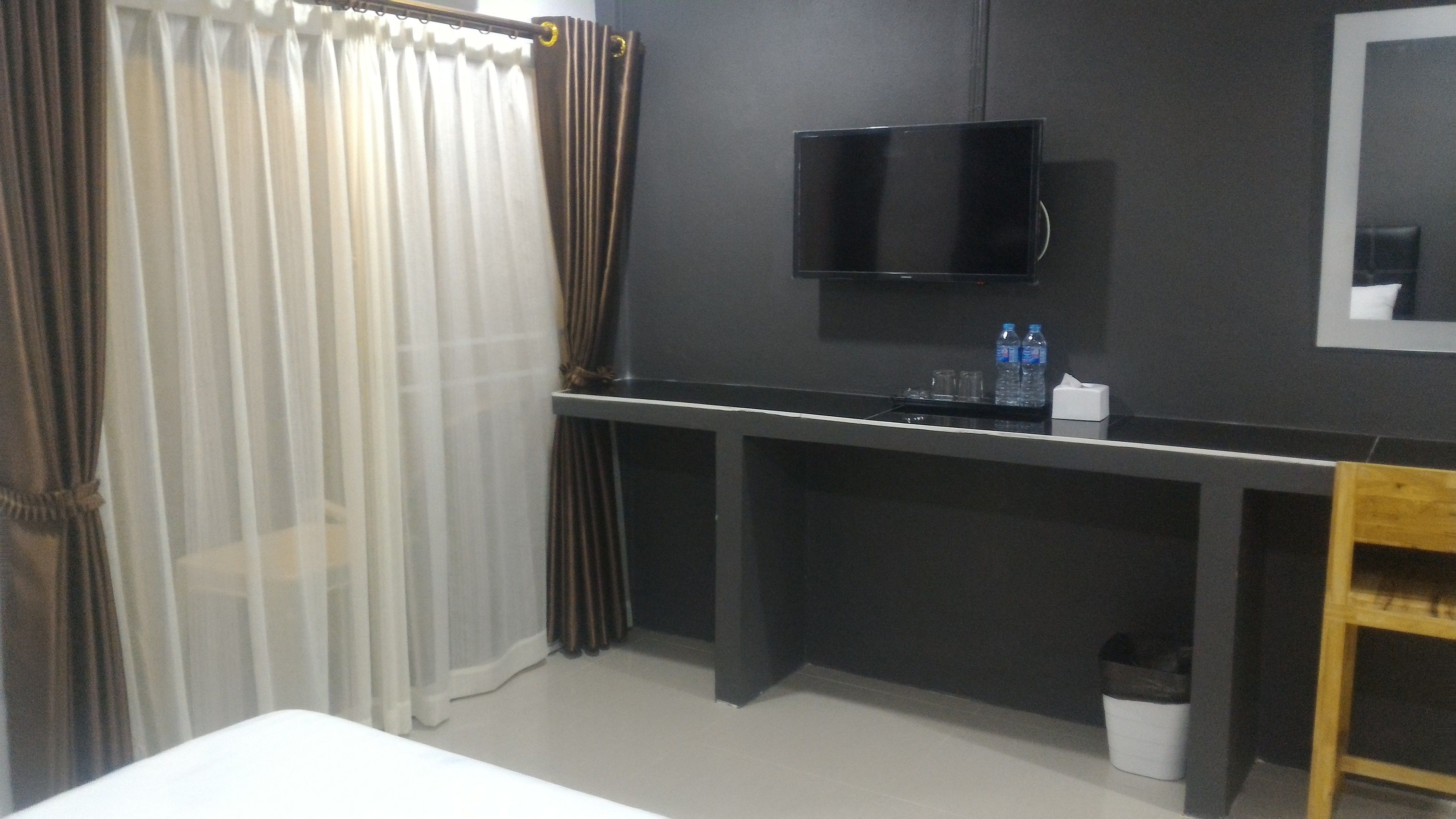 A hotel room with a bed, a desk with a flat-screen TV, a trash bin, and a water bottle on the desk.