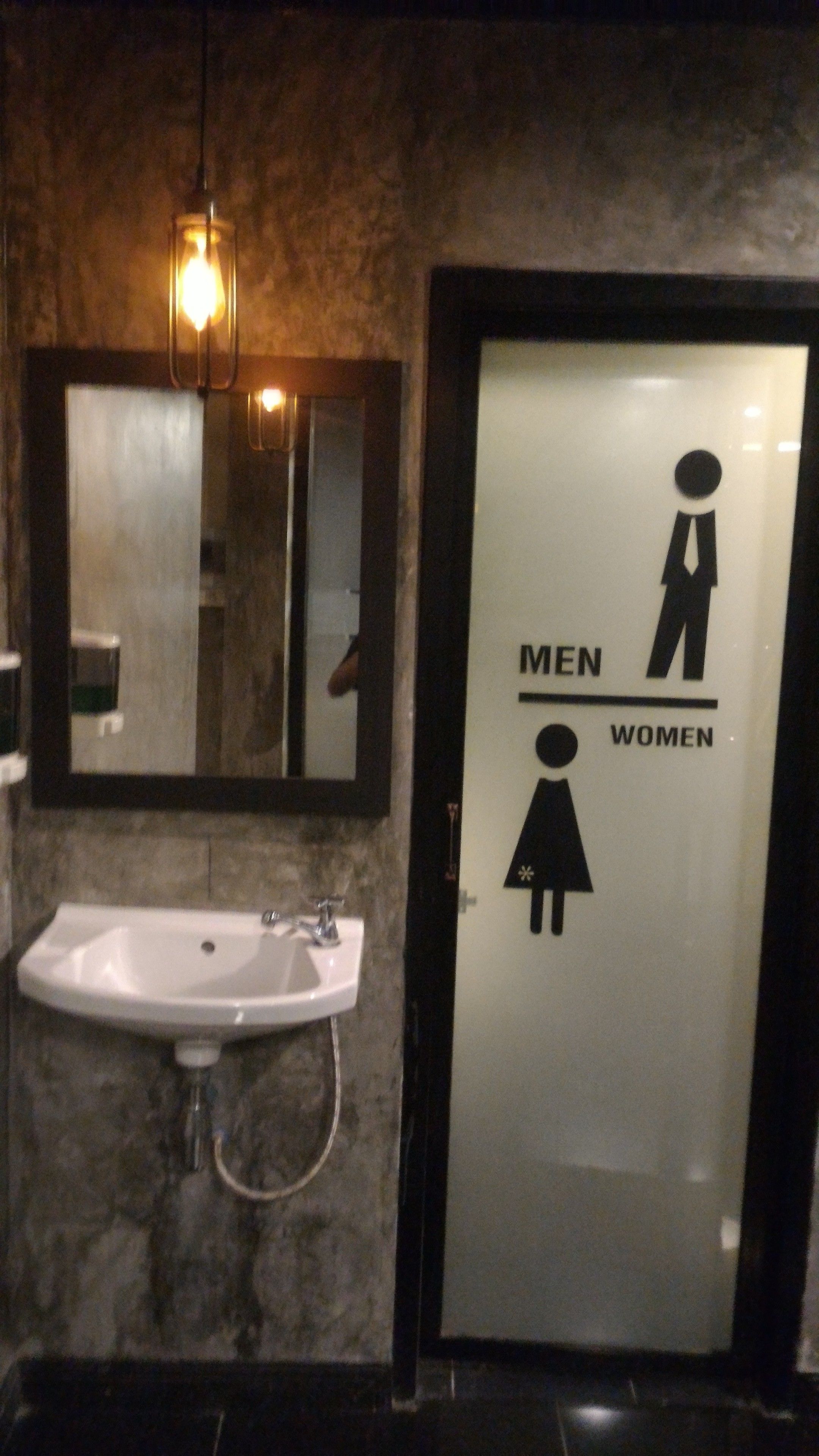A restroom with a sink, a mirror, and a door with gender symbols indicating men's and women's facilities.