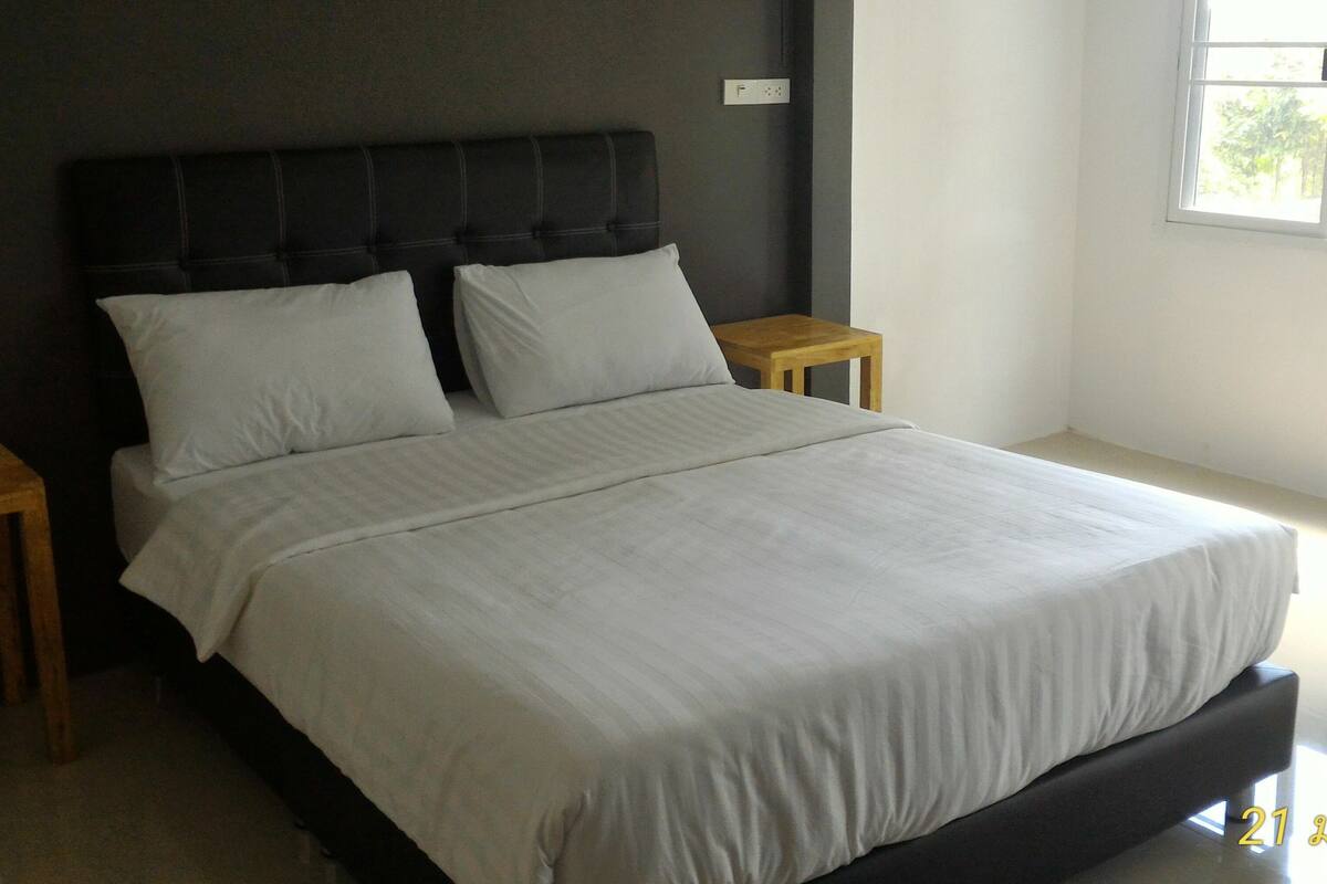 A bed with a dark headboard, two bedside tables, and a window with daylight coming through.
