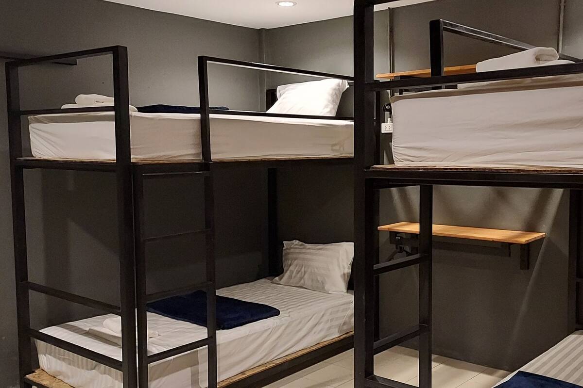 A bunk bed room with a wooden frame, white bedding, and a small shelf.
