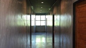 A corridor with metallic walls, a wooden door on the right, and a window at the end. - Loftel at Nakhon (Nakhon Si Thammarat)
