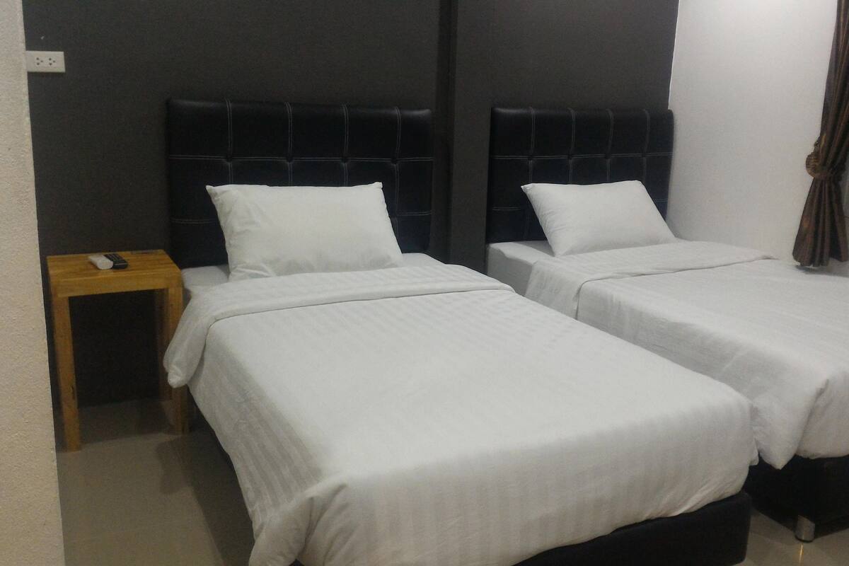 A hotel room with two single beds, a wooden nightstand, and a window with curtains.