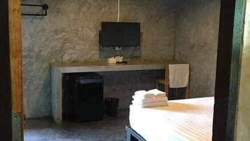 A compact hotel room with a bed, a small desk, a television mounted on the wall, and a trash bin.