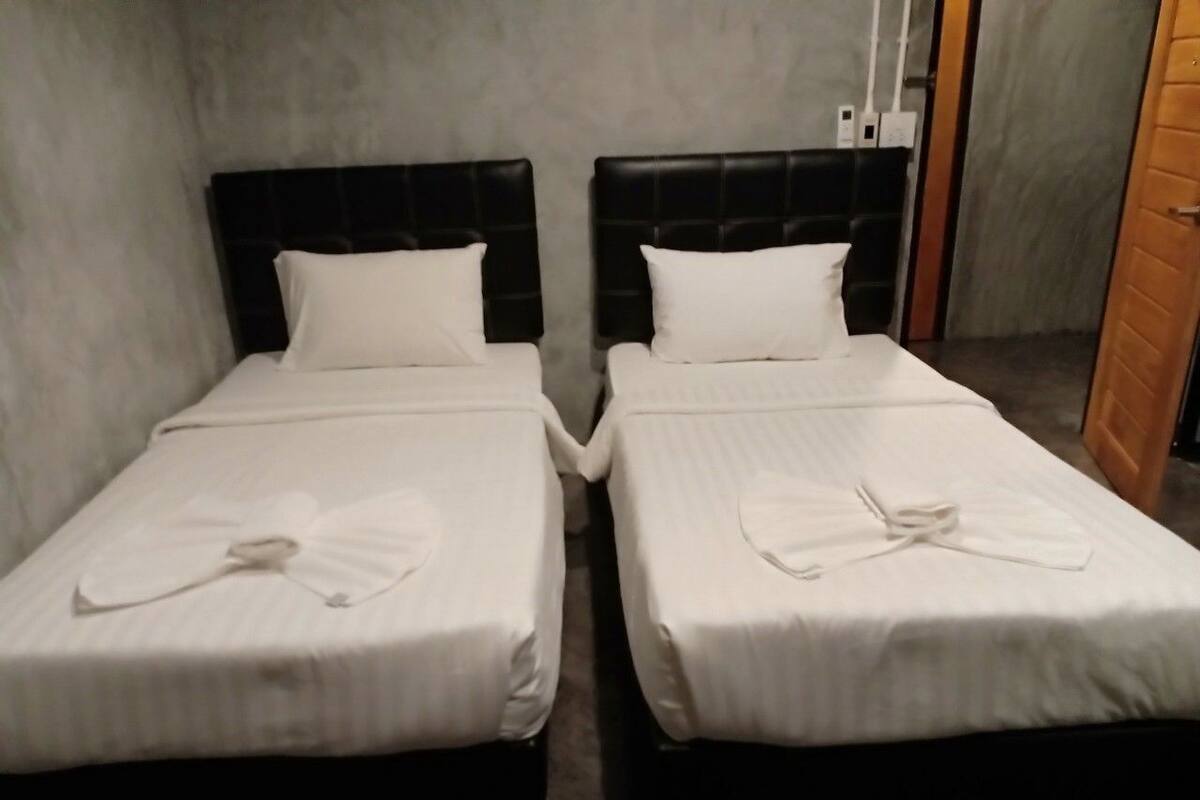 Two single beds with black headboards and white linens, a grey wall, and a wooden door.