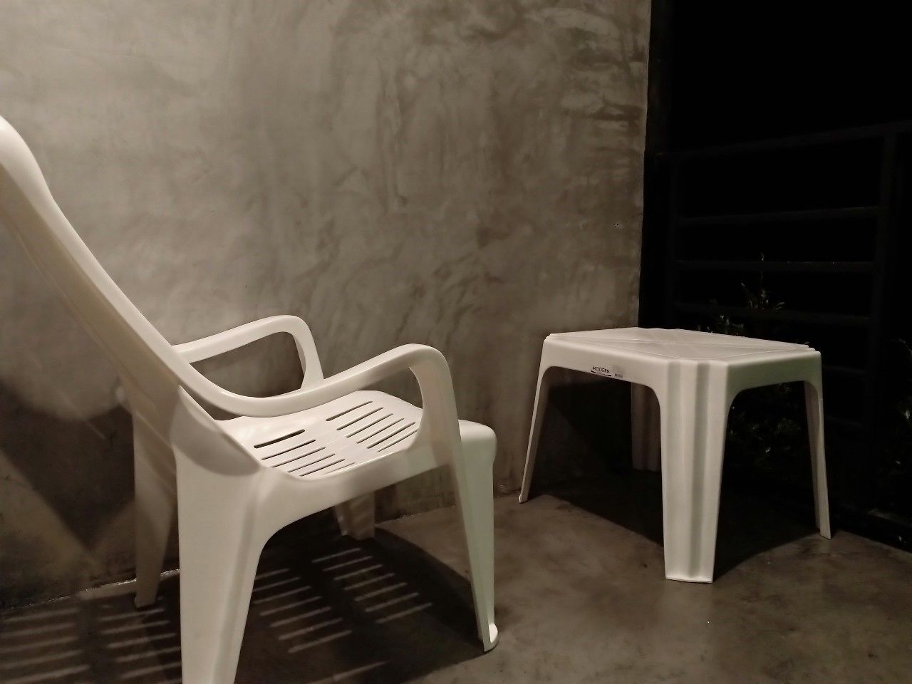 Una silla y un taburete blancos frente a una pared lisa.