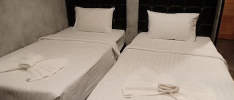 Two single beds with black headboards and white bedding, including neatly folded towels.