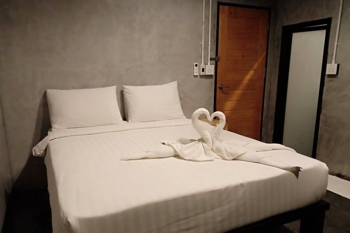 A neatly made bed with white linens and a towel arranged in a swan shape on the bed.