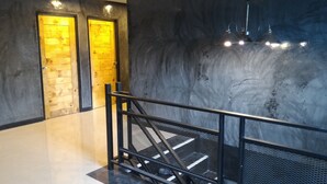 A modern interior with a metal staircase, a polished floor, and two wooden doors with a yellowish glow. - Loftel at Nakhon (Nakhon Si Thammarat)