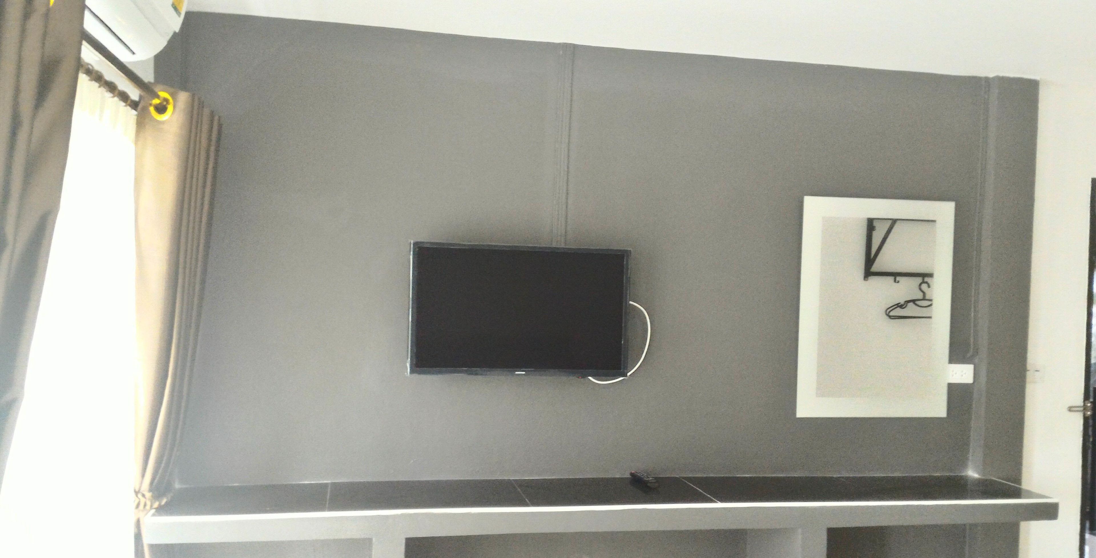 Una habitación con televisión de pantalla plana montada en la pared, un pequeño cuadro enmarcado y un escritorio de metal.