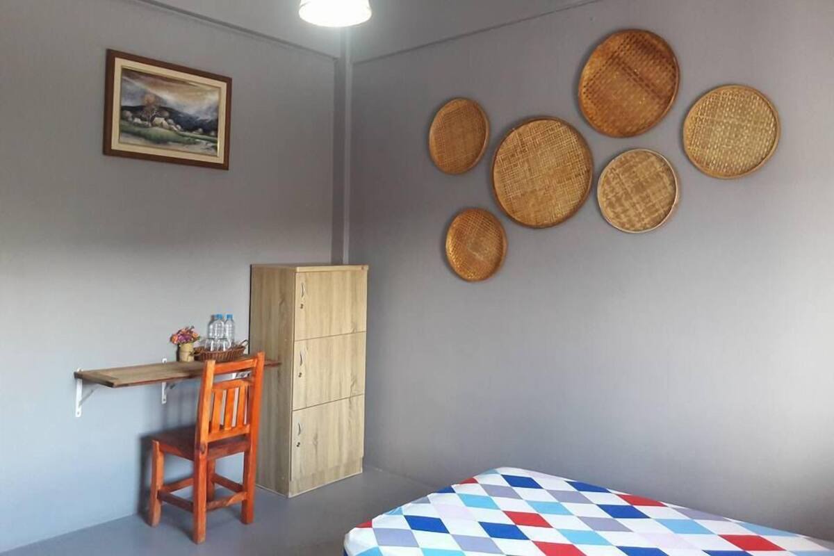 A room with a bed, a desk, a chair, a wardrobe, and a wall with woven baskets.
