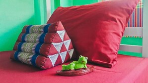 A bed with a red pillow and a patterned pillow, a small frog figurine, and a striped window view. - Muster House - Hostel (Ayutthaya)